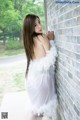 A woman in a white dress leaning against a brick wall.