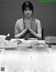 A woman sitting at a table with her hands clasped in prayer.