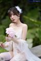 A woman in a white lingerie holding a pink flower.