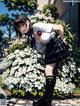 A girl in a school uniform standing in front of a flower bed.