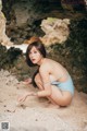 A woman in a blue bathing suit crouching on the beach.