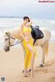 A woman in a yellow bikini standing next to a white horse.