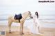 A woman in a white dress standing next to a horse on the beach.