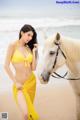 A woman in a yellow bikini standing next to a white horse.