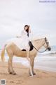 A woman in a white dress riding a horse on the beach.