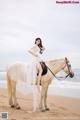 A woman in a white dress riding a horse on the beach.