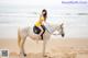 A woman in a yellow bikini riding a white horse on the beach.