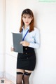 A woman in a blue shirt and black skirt holding a folder.