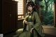 A woman in a green kimono sitting on a wooden floor.