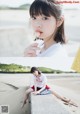 A young woman sitting on a concrete ledge eating a lollipop.