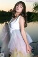 A woman in a white dress posing by a lake.