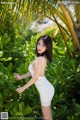 A woman in a white dress posing in front of a palm tree.