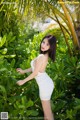 A woman in a white dress posing in front of a palm tree.