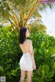 A woman in a white dress standing in front of a palm tree.