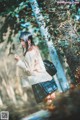 A woman in a school uniform is walking through the woods.