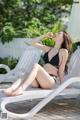 A woman in a black bikini sitting on a white lounge chair.