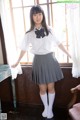 A woman in a school uniform posing by a window.