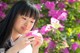 A young woman holding a pink flower in front of a bush of flowers.