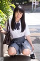 A young woman in a school uniform crouching down on the ground.