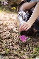 A woman kneeling down next to a flower in the woods.