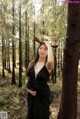 A woman in a black dress standing in the woods.