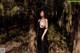 A woman in a black dress standing in the woods.