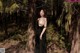 A woman in a black dress standing in the woods.