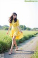 A woman in a yellow dress walking down a dirt road.