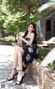 A woman in a black dress sitting on a stone wall.