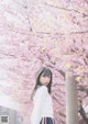 A woman standing in front of a tree with pink flowers.